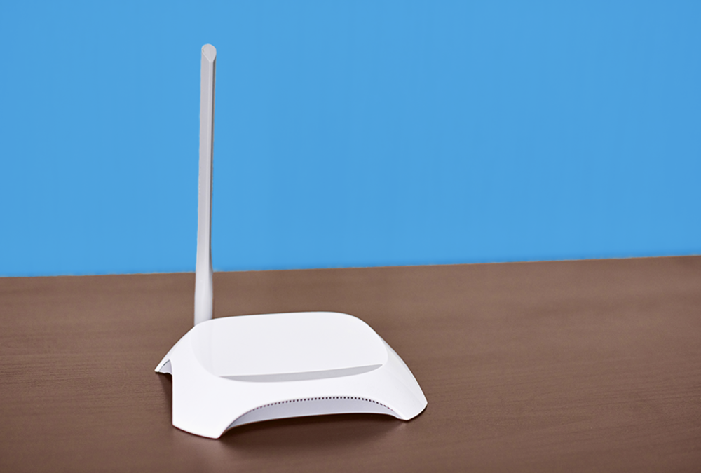 White WiFi router on brown desk with blue wall behind